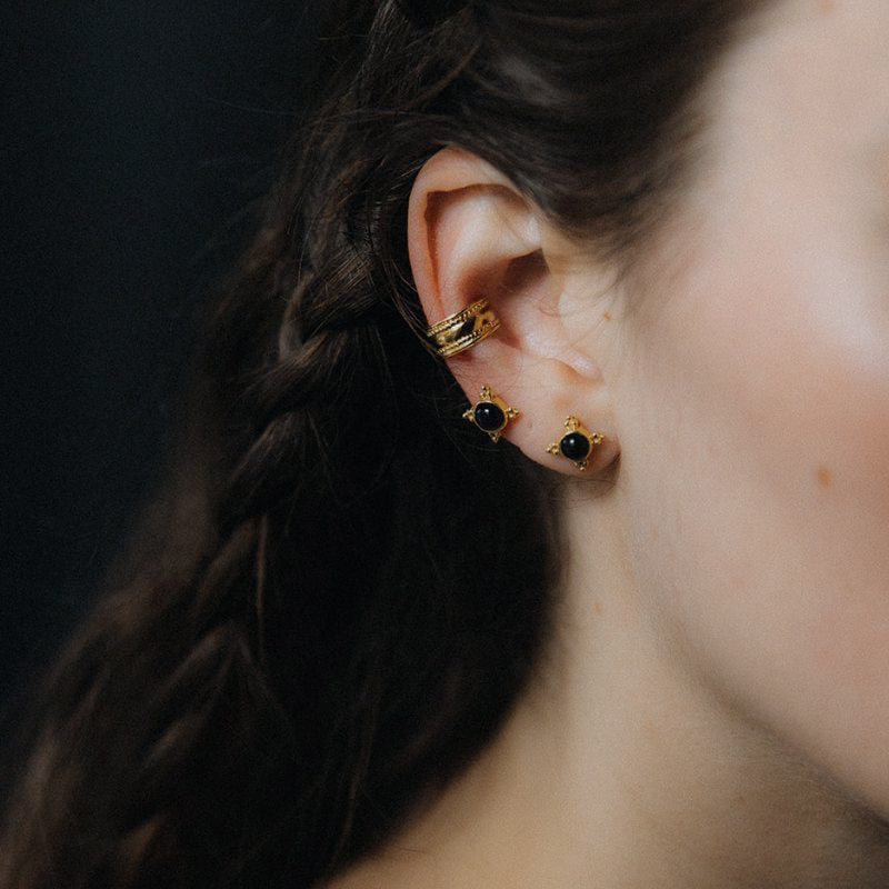 Gold stud earrings with black stones paired with a ridged ear cuff