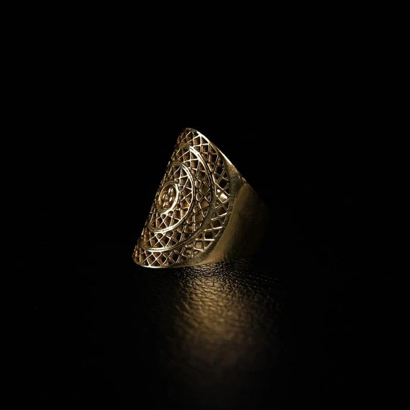 Handcrafted brass statement ring with open lattice filigree face and central sun motif, photographed against a black background.