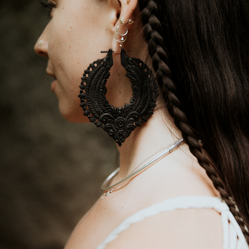  Woman wearing carved black wooden hoop earrings inspired by Bali jewelry traditions, shown in profile to highlight intricate carving and texture.