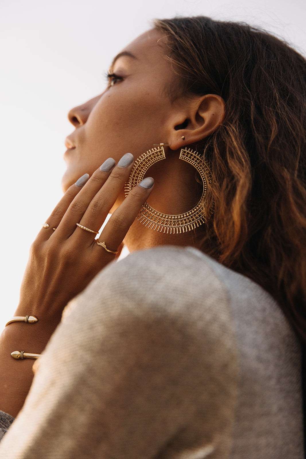 Gold hoop earrings paired with stacked rings and a cuff bracelet, profile view 