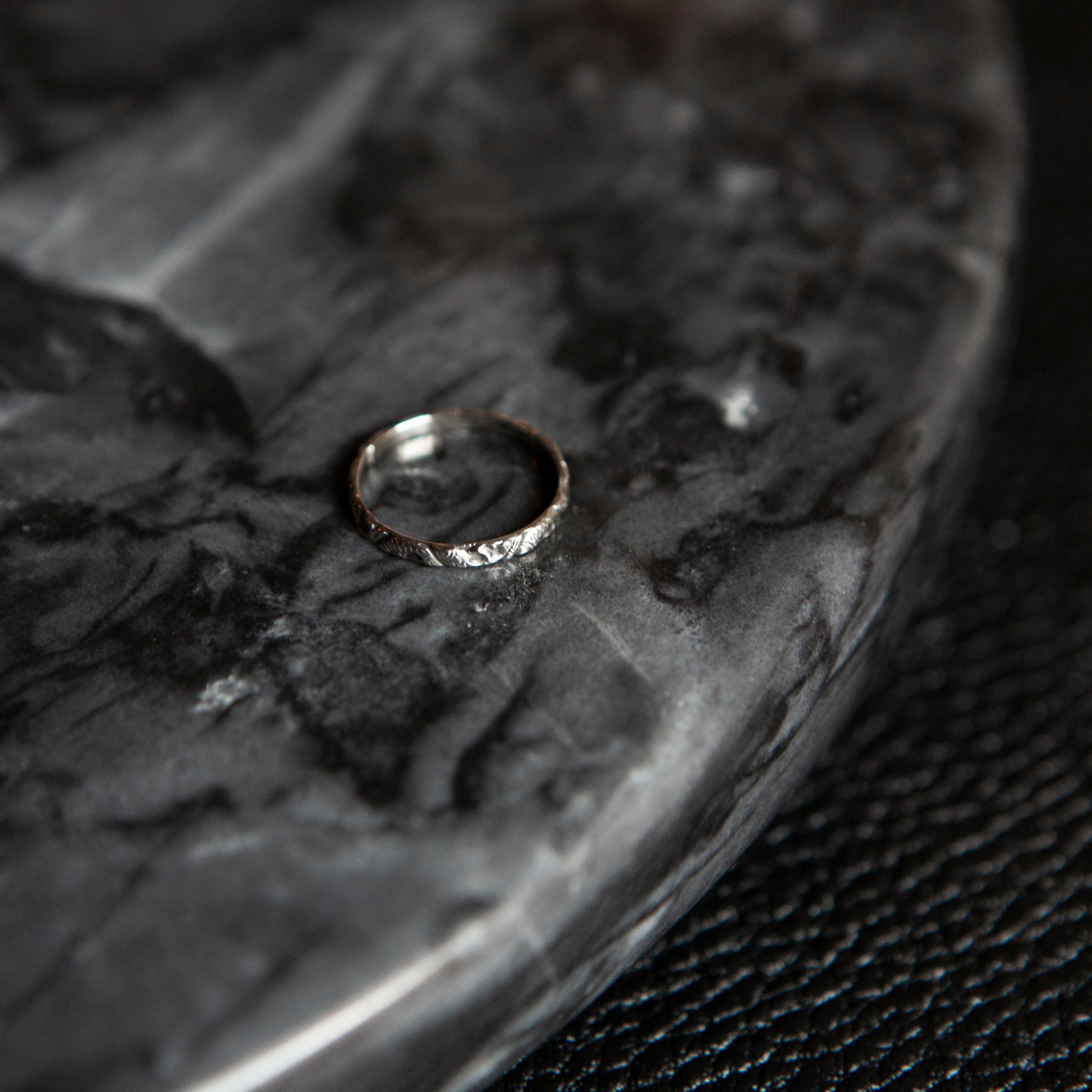 Thin 925 sterling silver stacking ring with hammered texture resting on a dark marbled ceramic surface, product shot.