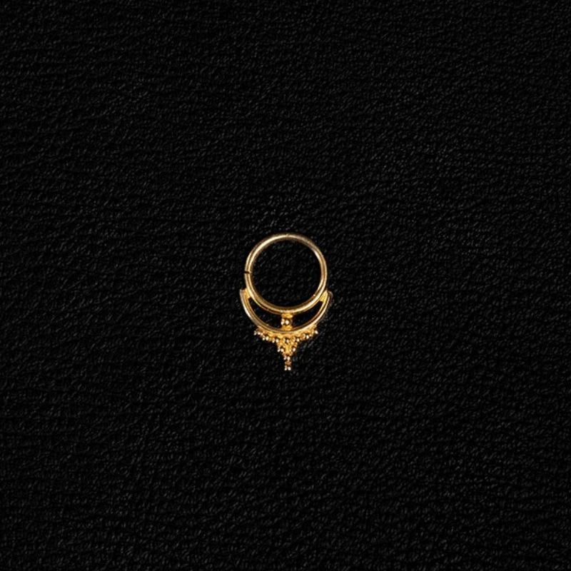 Gold septum jewelry ring with a double band and beaded granulation detail at its base, photographed against black textured leather