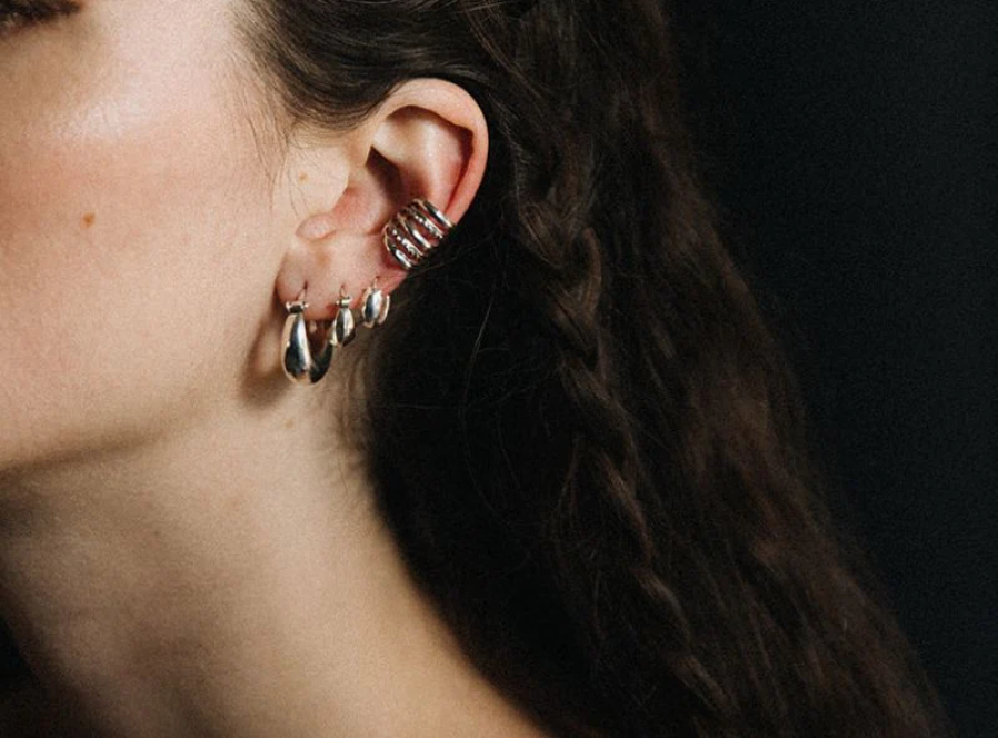 A woman wearing  gold huggie earrings Canada that have a beaded hoop at the first piercing with a small huggie above by Noir KĀLA.